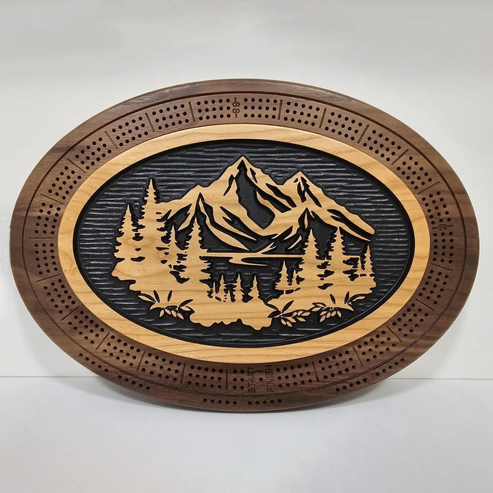 A handcrafted cribbage board featuring a scenic design of mountains, flowing water, and lush trees.
