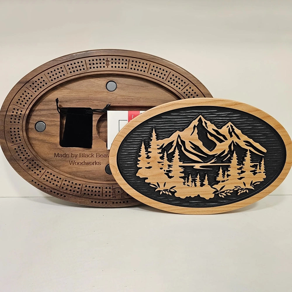 A handcrafted cribbage board featuring a scenic design of mountains, flowing water, and lush trees.