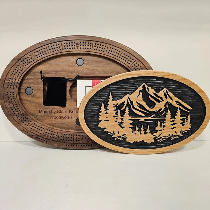 A handcrafted cribbage board featuring a scenic design of mountains, flowing water, and lush trees.