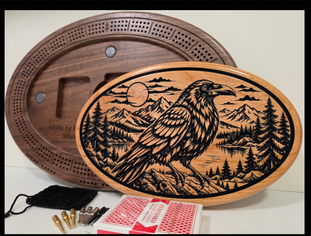 Oval wooden cribbage board with raven and mountain artwork, shown with the scoring board, storage compartments, cards and pegs.