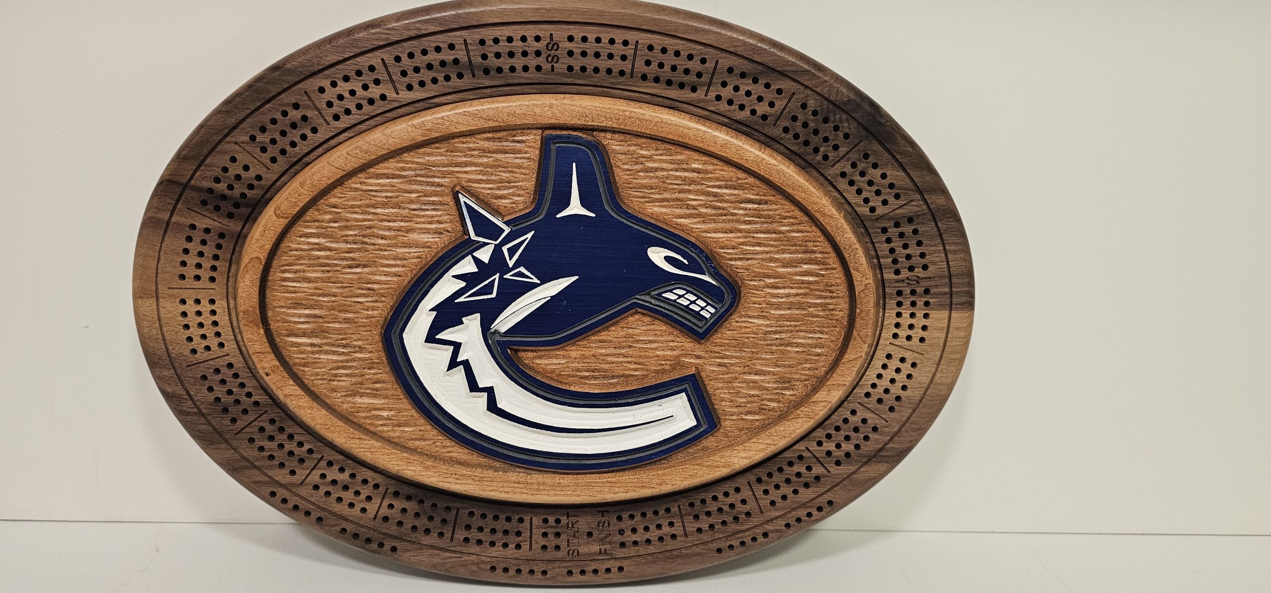 Vancouver Canucks oval wooden cribbage board with team logo and decorative carved border on white background.